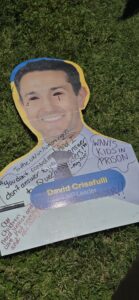 Invasion Day Rally Meanjin Brisbane 2026. Signs lay on the grass before the march. A cutout of David Crisafulli's core flute campaign ad.